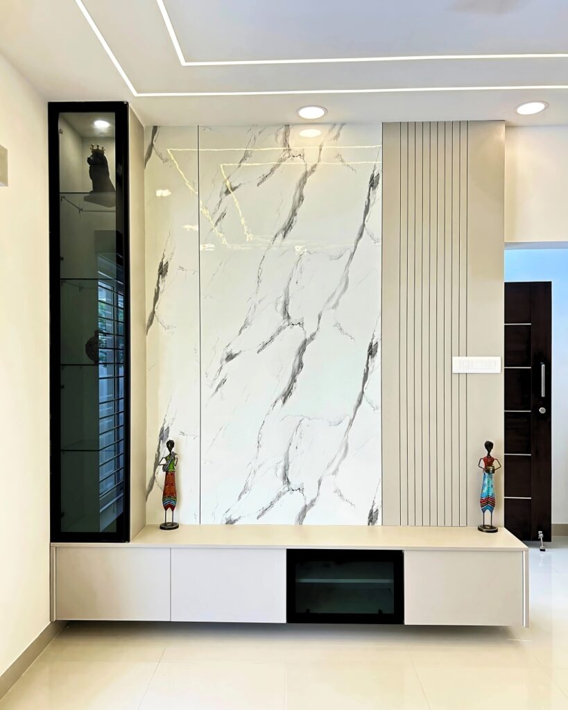 Stylish TV unit with marble effect panel and floating storage designed by the best interior designers in Chennai for a modern 3BHK villa